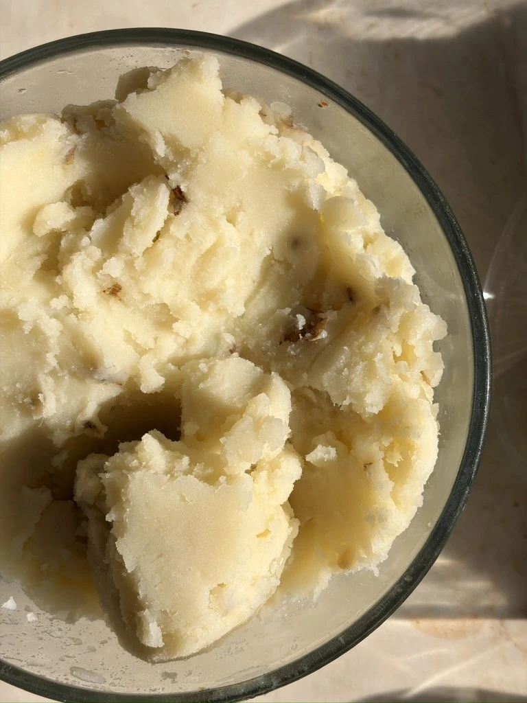 A bowl of creamy dairy-free garlic mashed potatoes topped with fresh parsley and cracked black pepper, showing a smooth, fluffy texture and light golden color from olive oil and garlic.