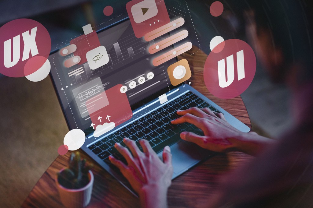 Hands typing on a laptop with floating UI and UX design elements around the screen.