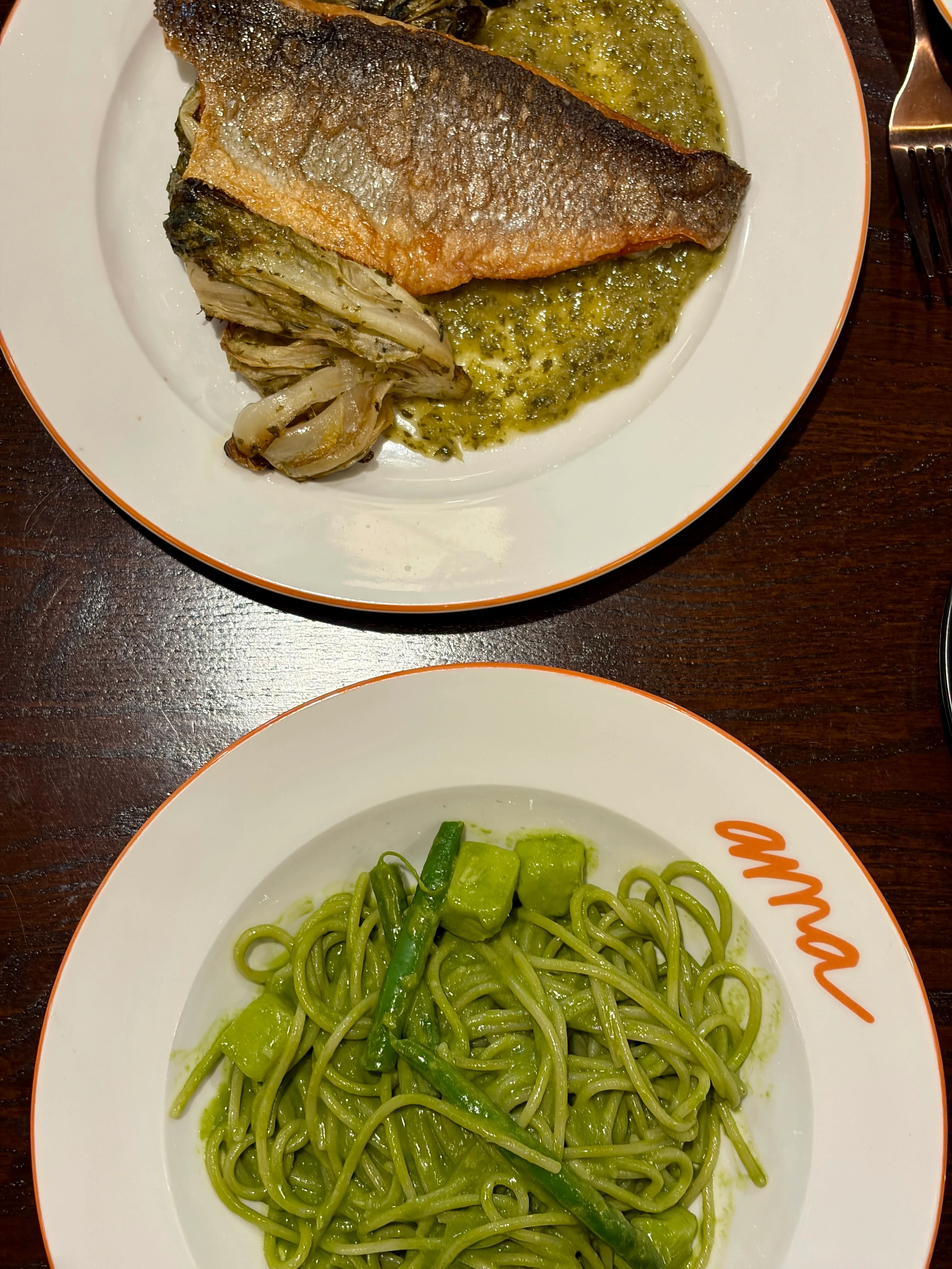Ama restaurant meal with grilled branzino fish and pesto pasta on white plates