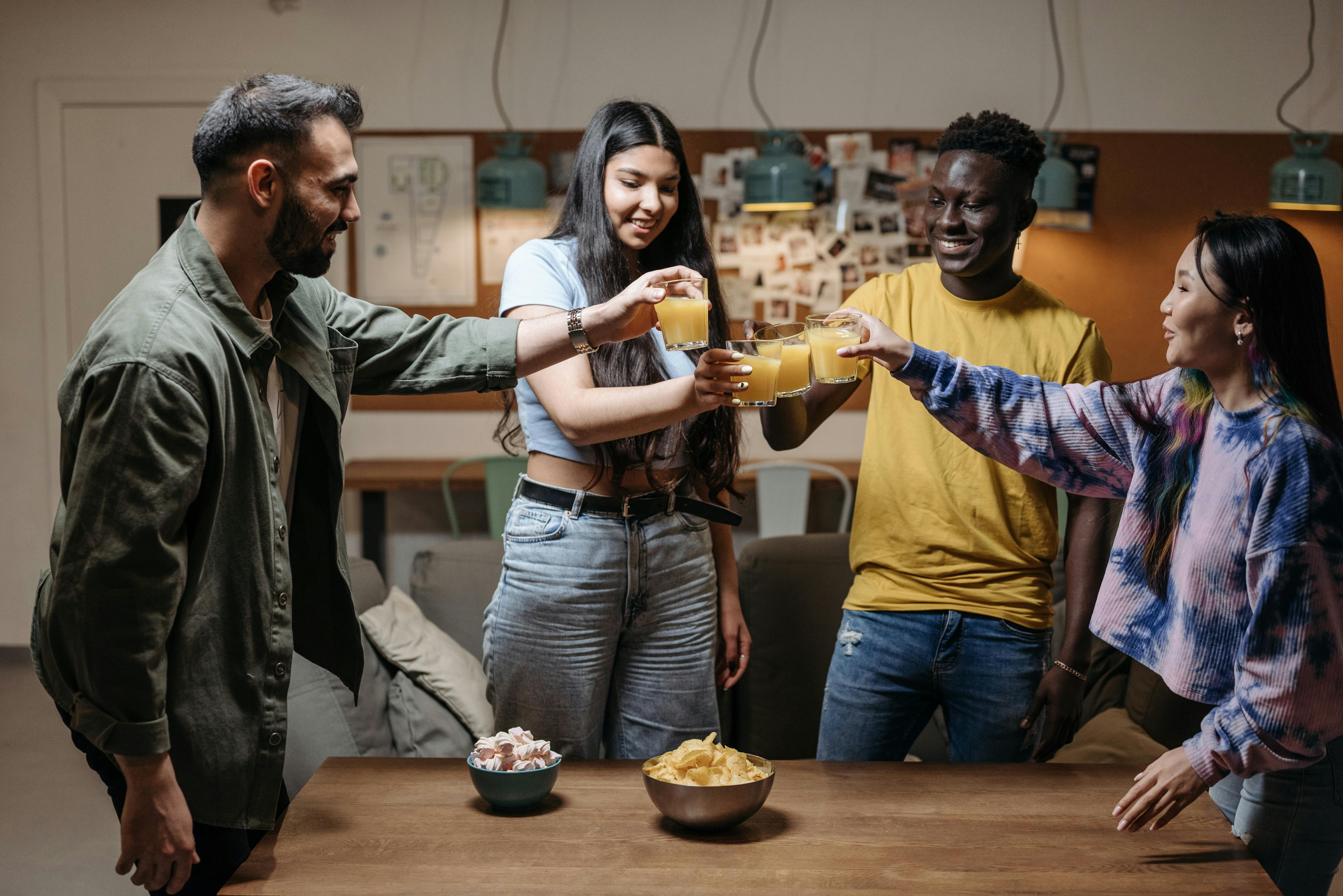 A group of four young adults from diverse backgrounds smiling and toasting with glasses of orange juice in a cozy, modern apartment, with snacks on the table—capturing a friendly and welcoming atmosphere, ideal for new residents settling into life in Berlin.