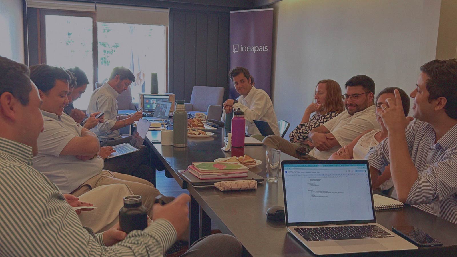 Portada de Club de lectura, programa de formación de IdeaPaís, mostrando a un grupo de personas que comparte sentados alrededor de una mesa. 