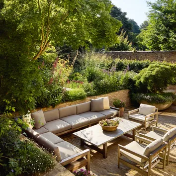 A cozy outdoor seating area surrounded by lush greenery, featuring a wooden table and comfortable sofas.