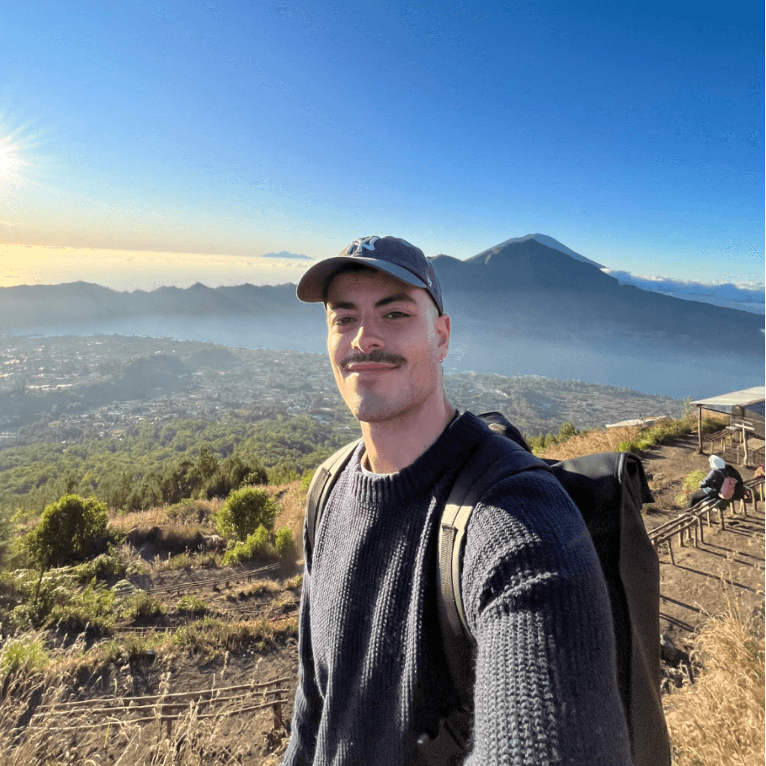 A pselfie of Luke - founder of hamilton solutions on top of Mount Batur in Ubud, Bali wearing a navy jumper and a navy baseball cap at sunrise.
