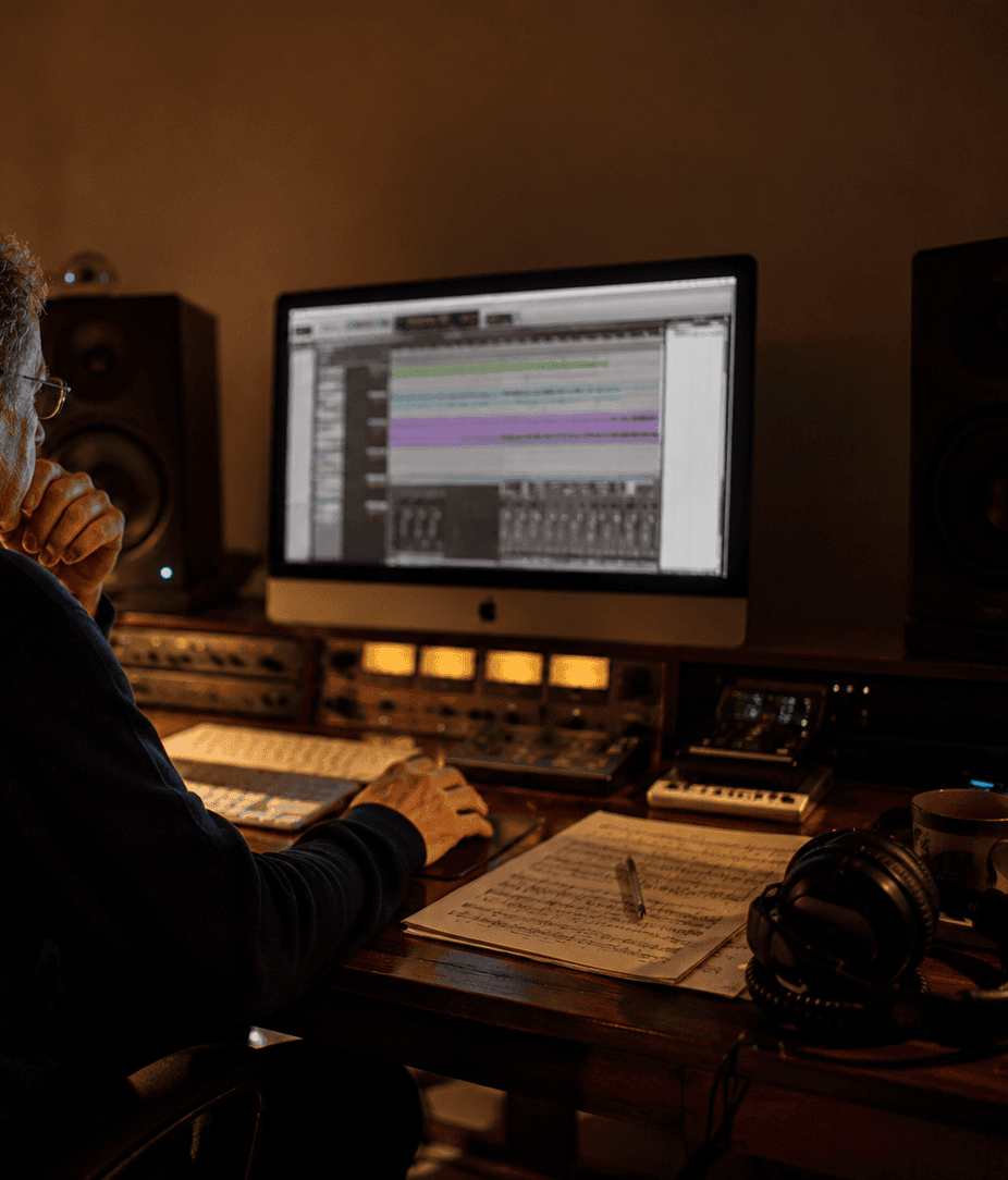 Persona al computer con cuffie e spartito musicale.