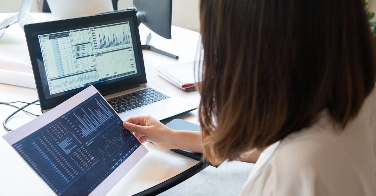 A professional woman analyzes financial charts on a laptop and paper for business insights.