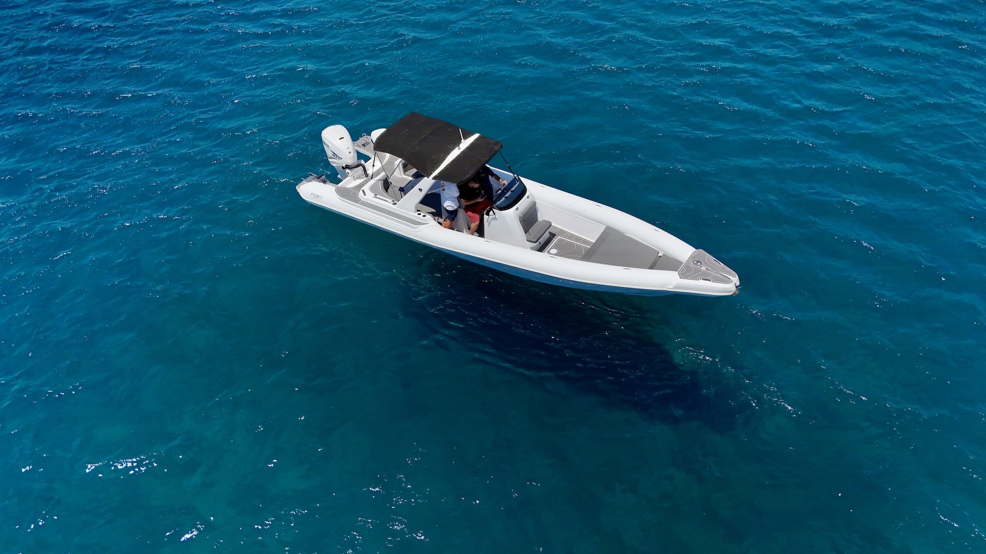 White Fost Matrix 32 rigid inflatable boat with black T-top canopy anchored in crystal-clear turquoise waters of the Aegean Sea.