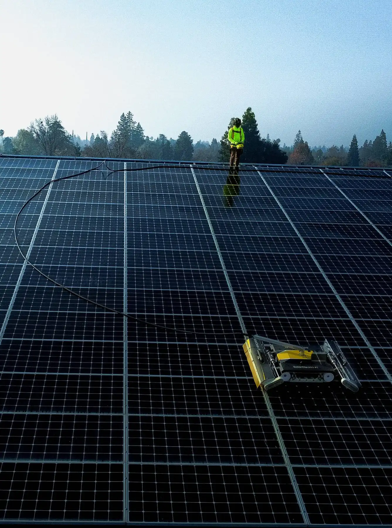 Technician with a robotic panel cleaner on a large ground-mount array at dawn | Premier Solar Service, serving Fresno, CA