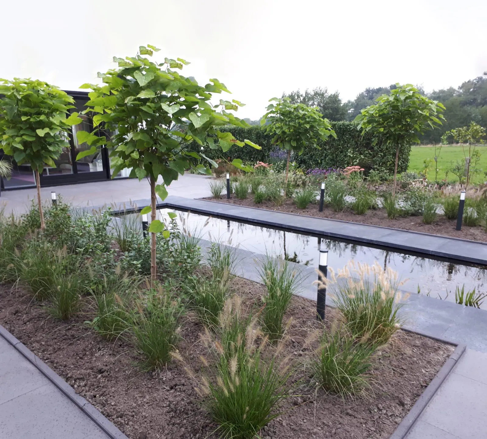 Prachtige tuin met strakke tuin tegels met groene borders en strook water