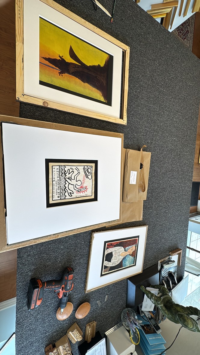 Assorted framed artwork staged for installation, including a Keith Haring print and a modern portrait