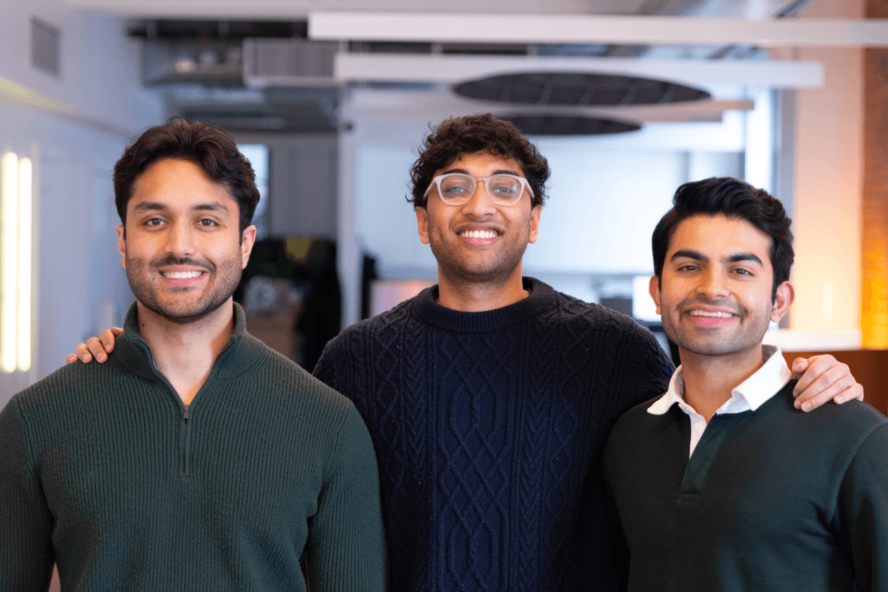 Three smiling young men, likely business partners or investors, stand together in a modern office environment.