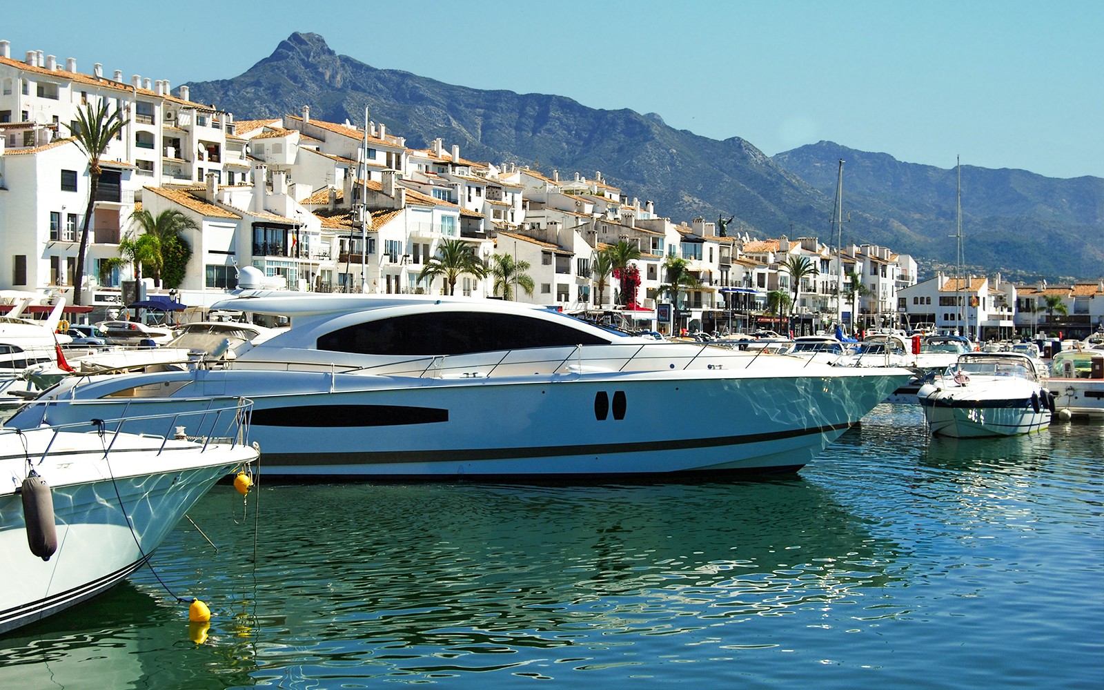Yachts docked at Puerto Banús marina with mountains in the background.
