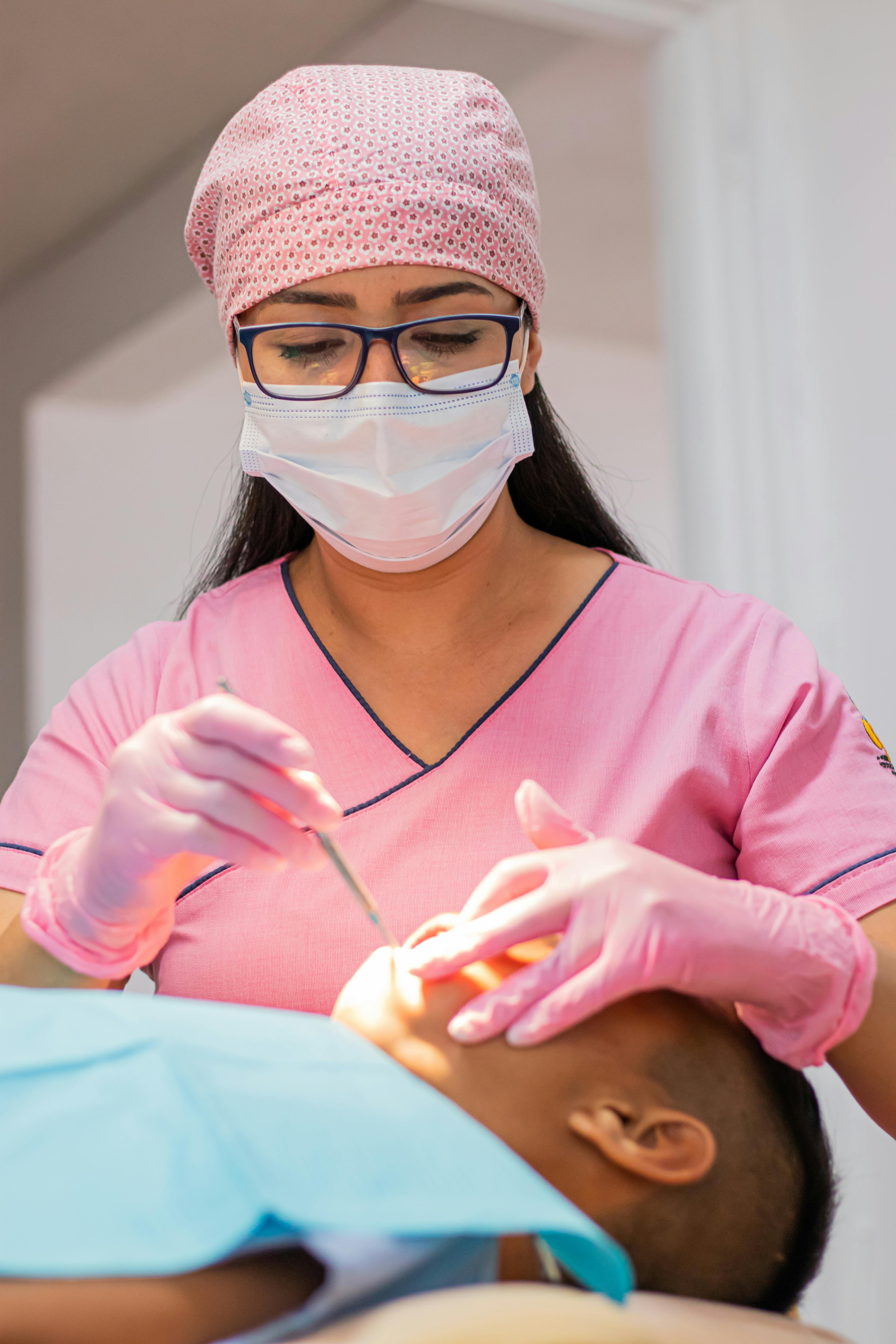 Healthcare worker in blue scrubs adjusting gloves in clinical setting with green curtains and equipment