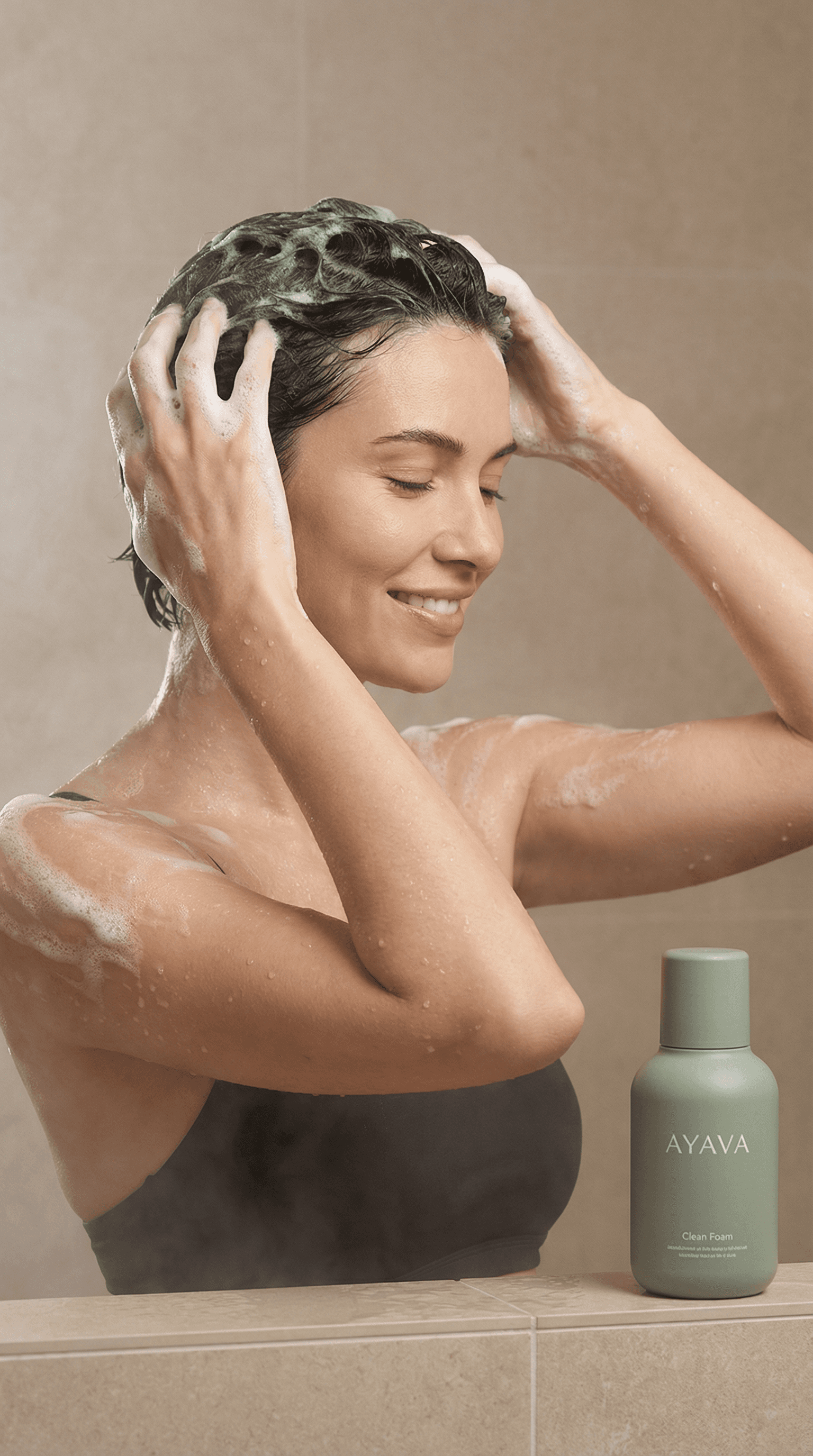Model washing hair in shower with AYAVA Clean Foam bottle on ledge