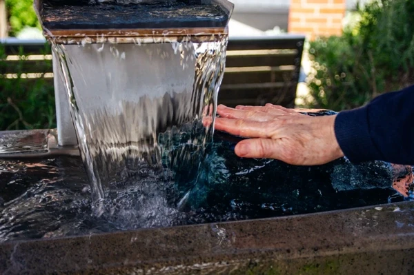 Hand reaching into flowing water at an outdoor fountain