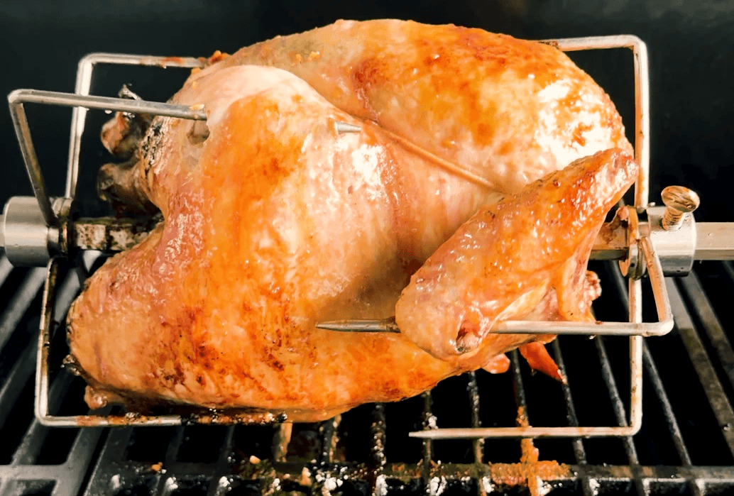 A whole chicken on a rotisserie being grilled