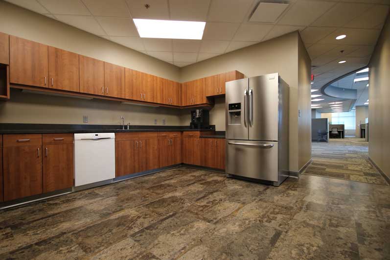 A modern kitchen space with wooden cabinets, stainless steel appliances, and tiled flooring. Bright lighting is overhead.