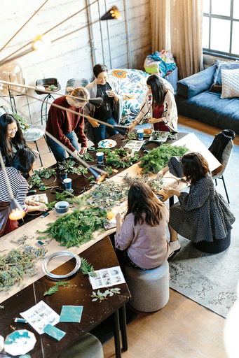 Aerial view of people gathered around a table, working together with plants and materials in a cozy indoor setting.