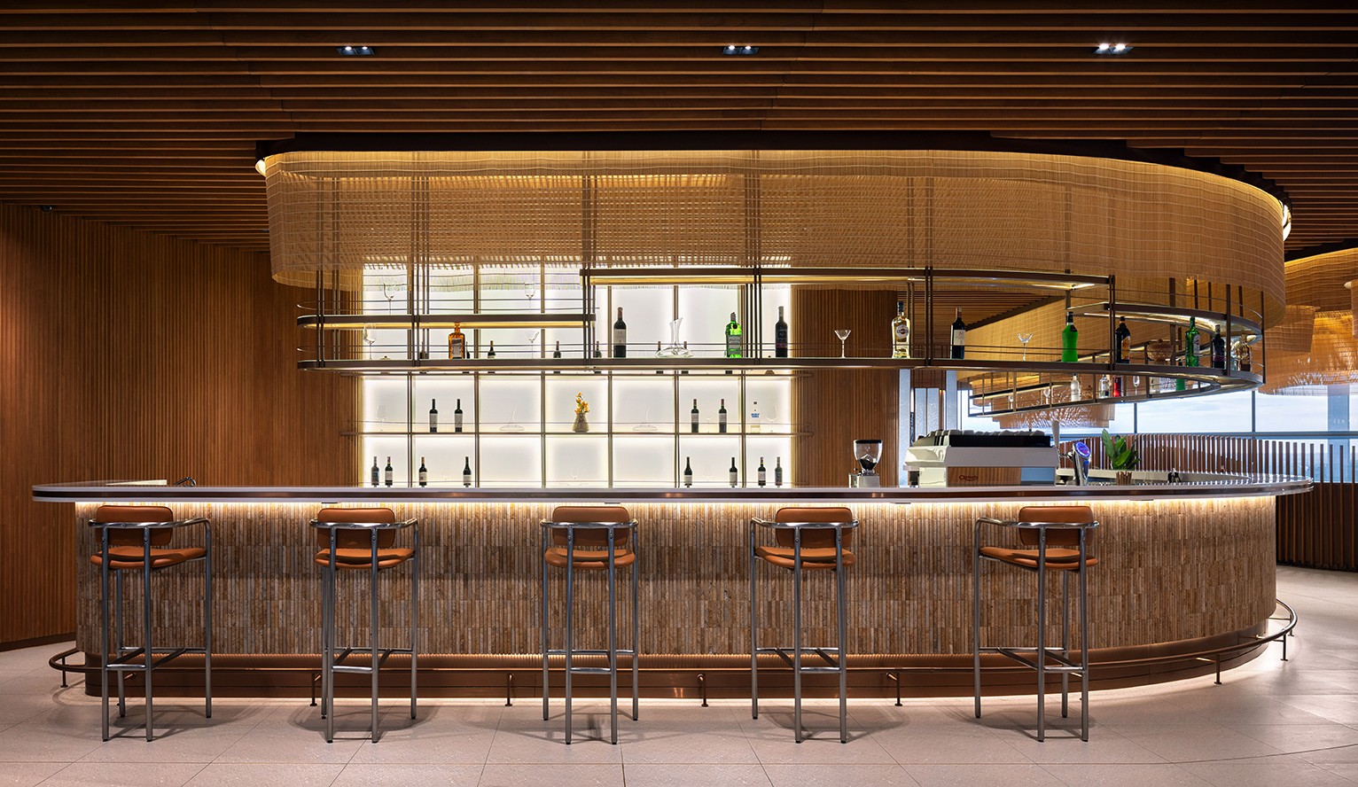 Architectural shot of the circular bar counter with backlit tiered bottle displays and timber finishes highlighting the intersection of operational efficiency and superior interior finishing