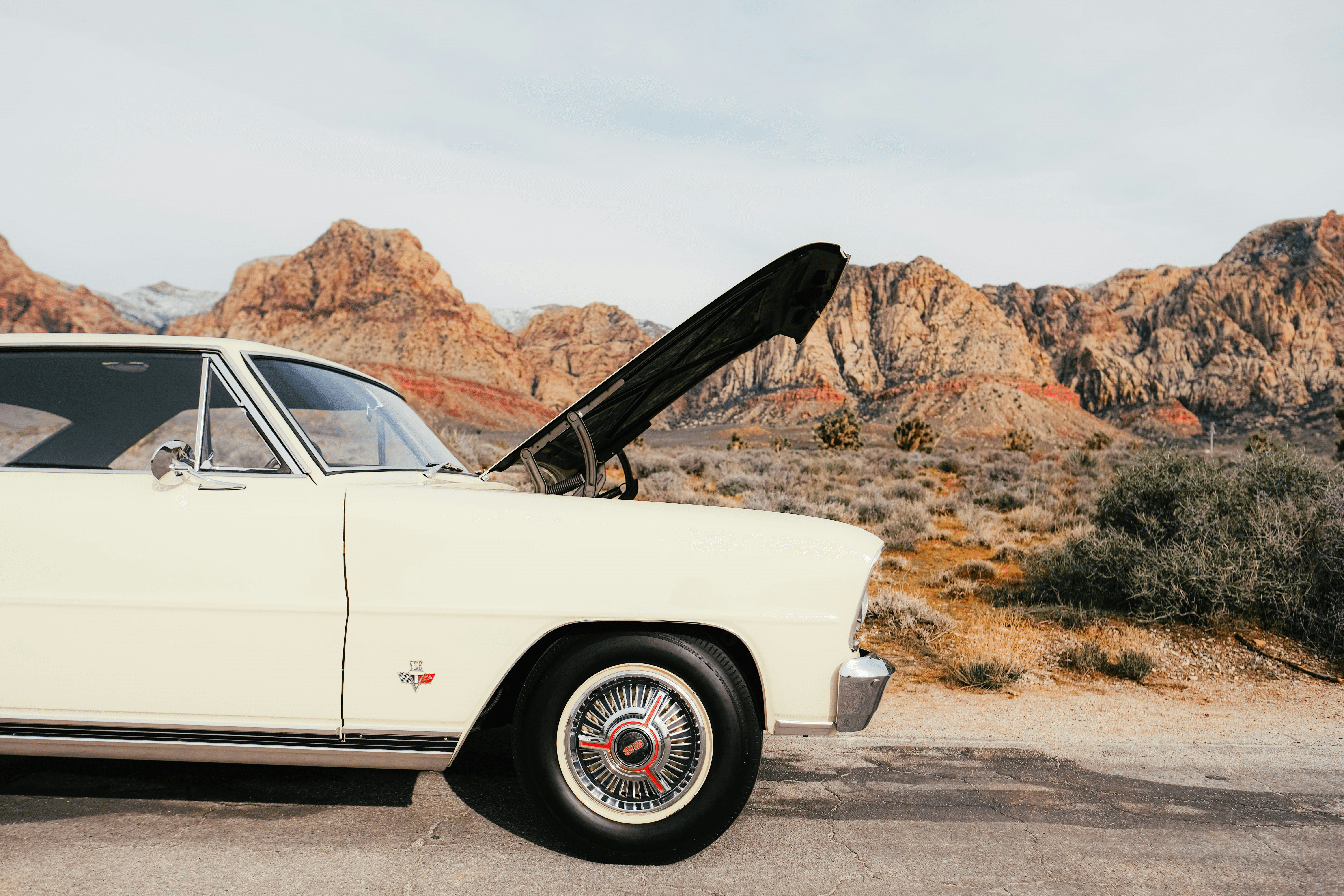 Classic car with open hood in desert landscape.