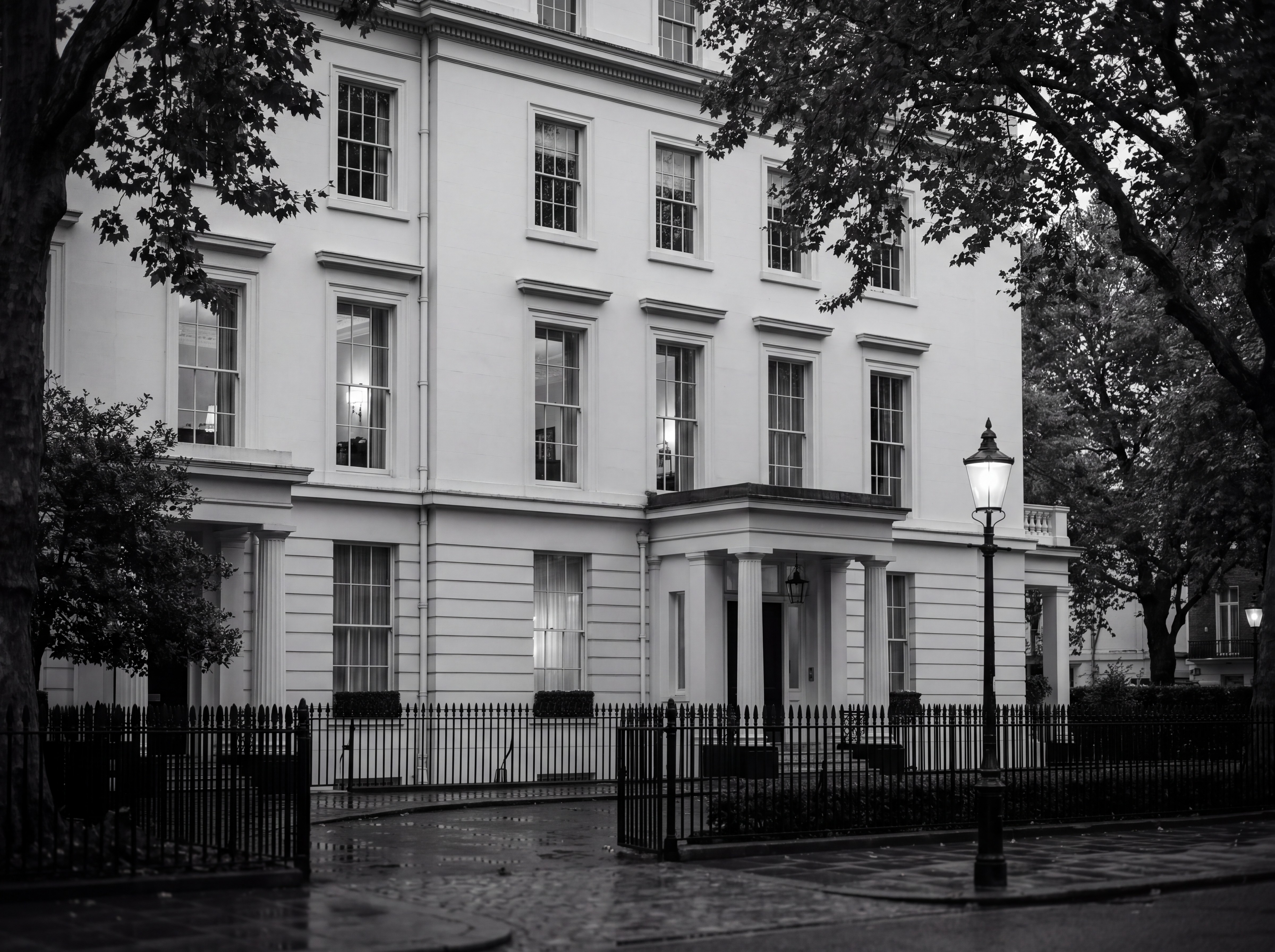 Grand white stucco mansion in Prime Central London at dusk behind iron railings, illustrating the proposed non-resident mansion tax premium on high-value property, monochrome editorial photograph