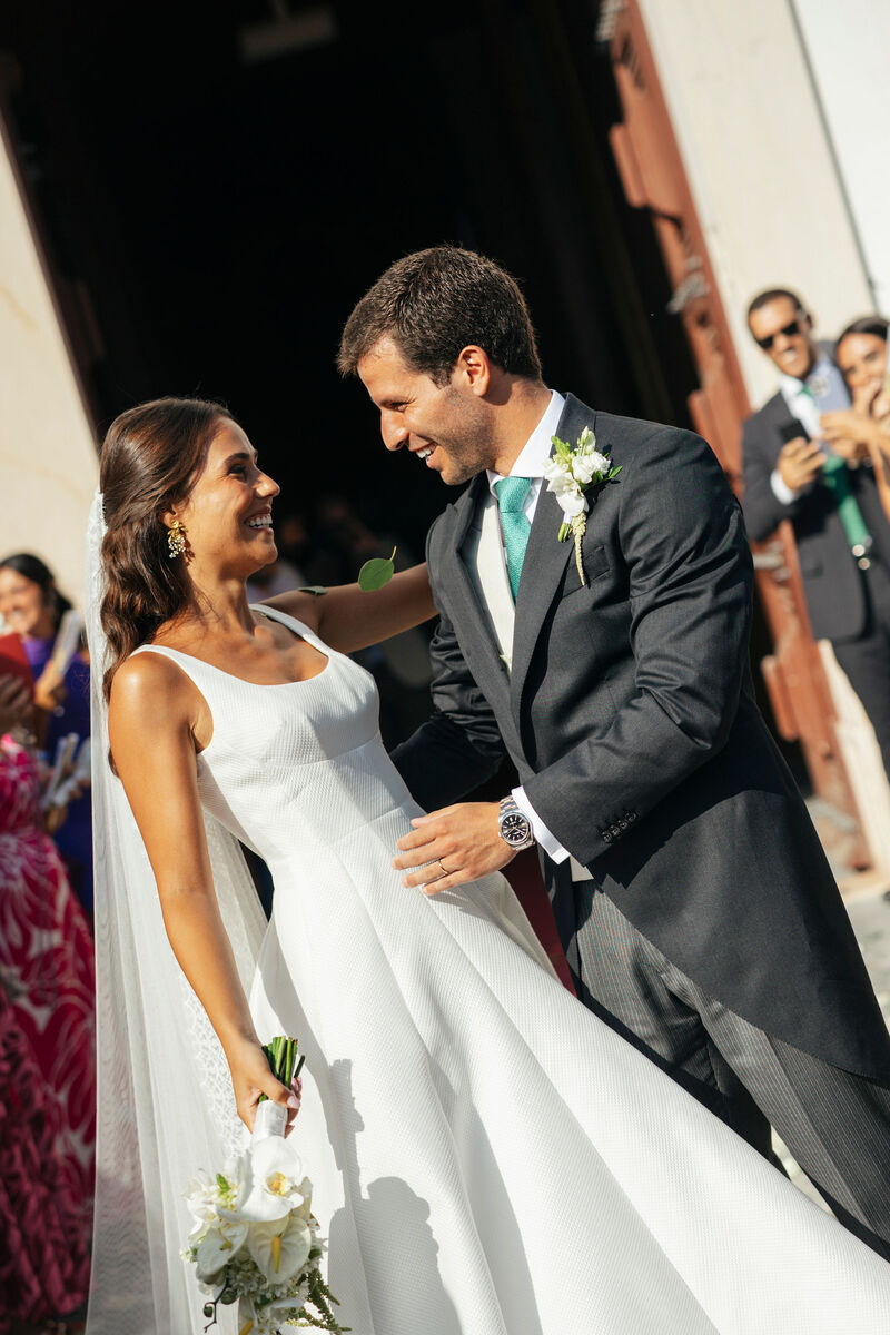 Bride and groom smiling at one another outside a church
