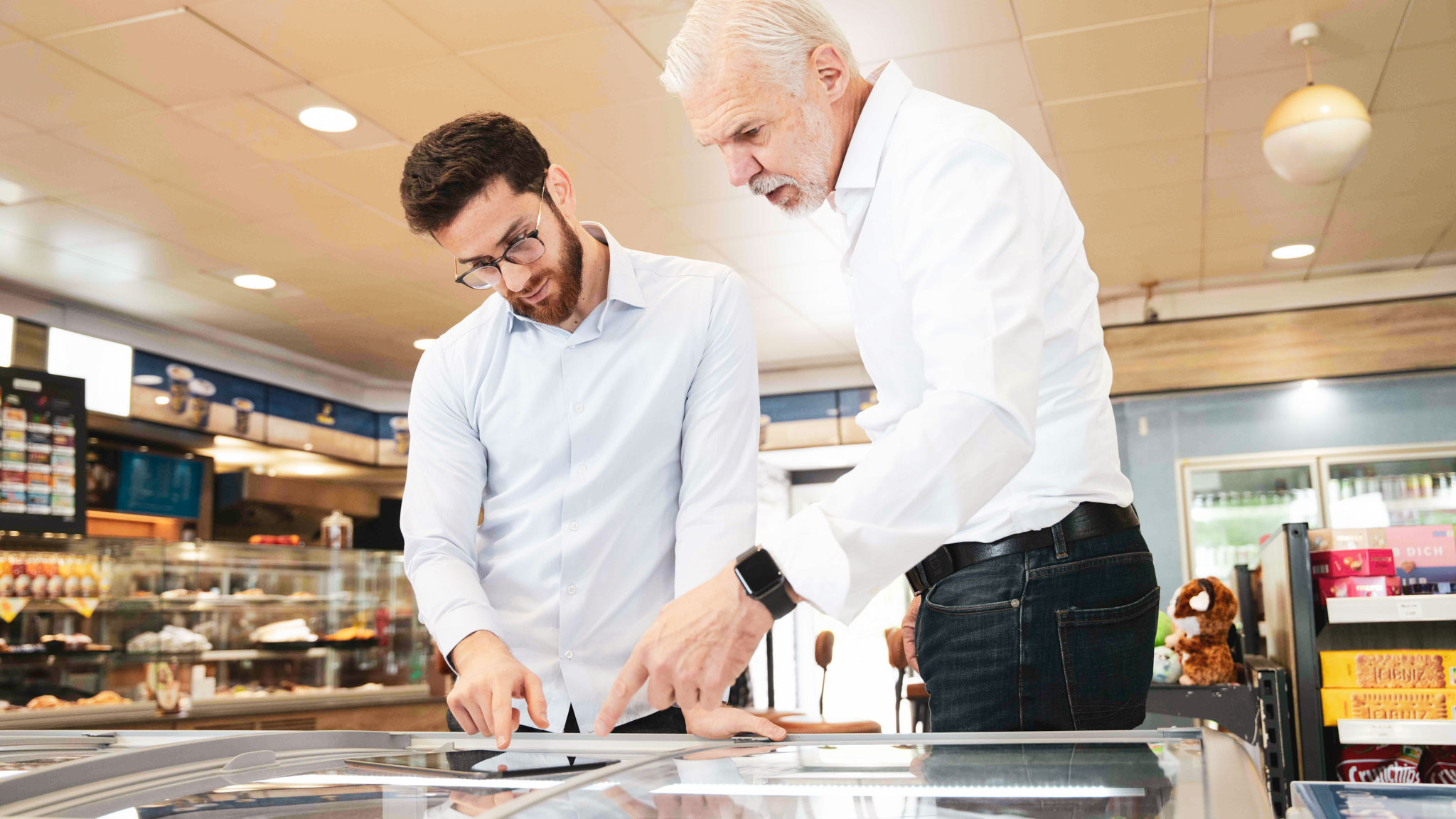 Zwei Männer im Gespräch über Verkaufsstrategien – konzentriert analysieren sie Unterlagen auf einem Tisch. Moderne, lichtdurchflutete Umgebung unterstreicht den professionellen Austausch und Teamgeist im Vertrieb.