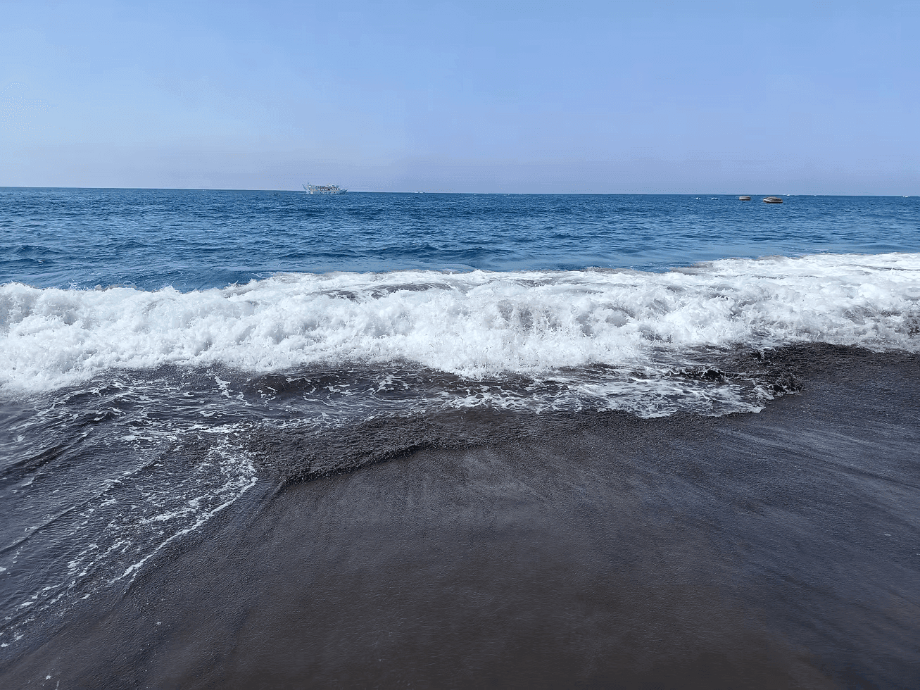 Wellen am schwarzen Strand, blaues Meer und Himmel. Sommerurlaub.