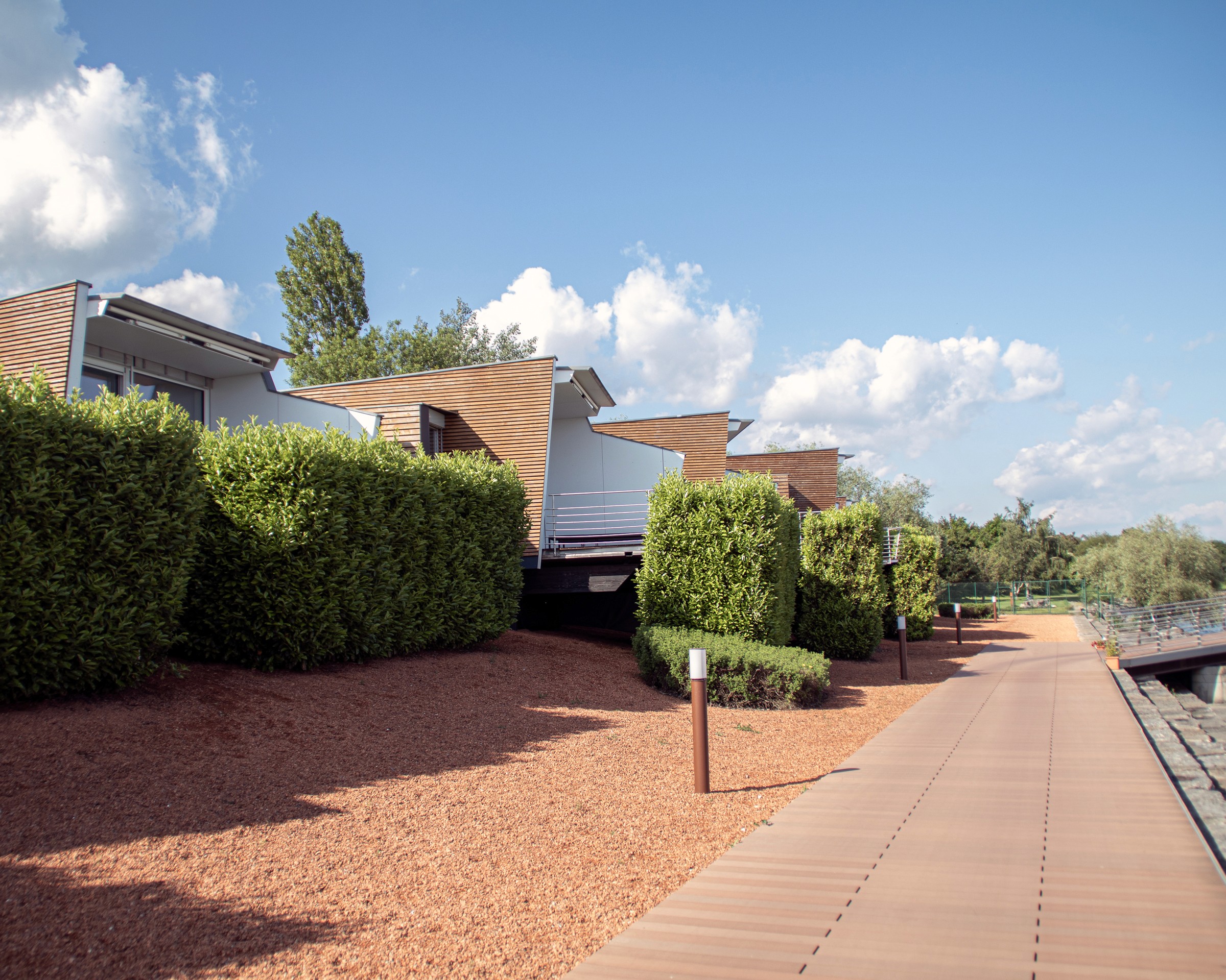 Photo architecturale de la promenade le long du lac de Neuchâtel qui abrite les bungalows terrestres de l'hôtel Palaffite parsemés de haies vertes