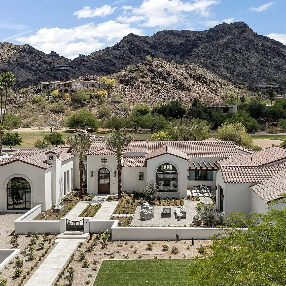 Luxury white stucco home with tile roof, surrounded by desert landscaping and mountains.