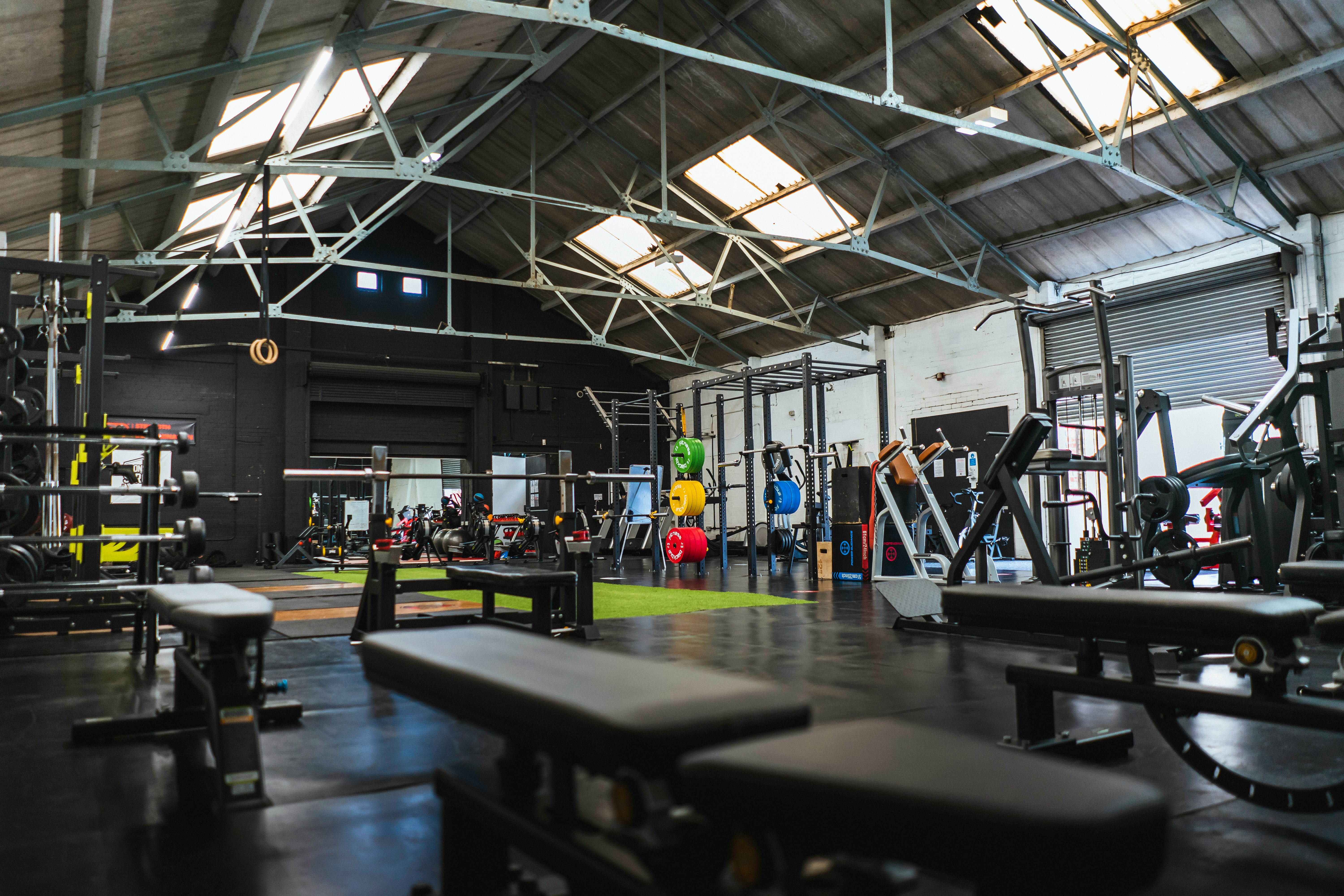 Weightlifting equipment and benches in a spacious industrial gym with a high ceiling
