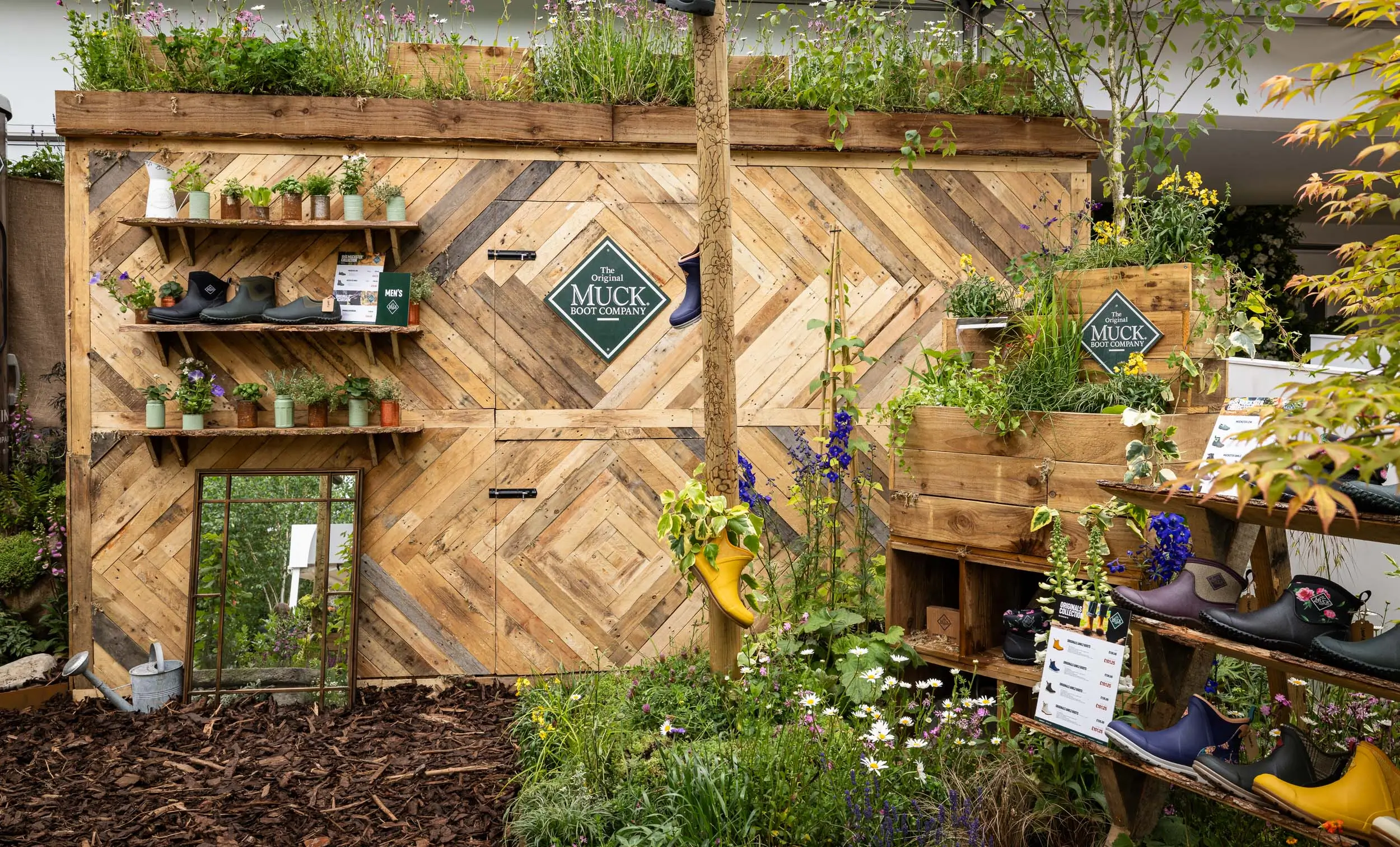 A lush green garden surrounds a textured, wooden building with balconies and vibrant plants adorning it.