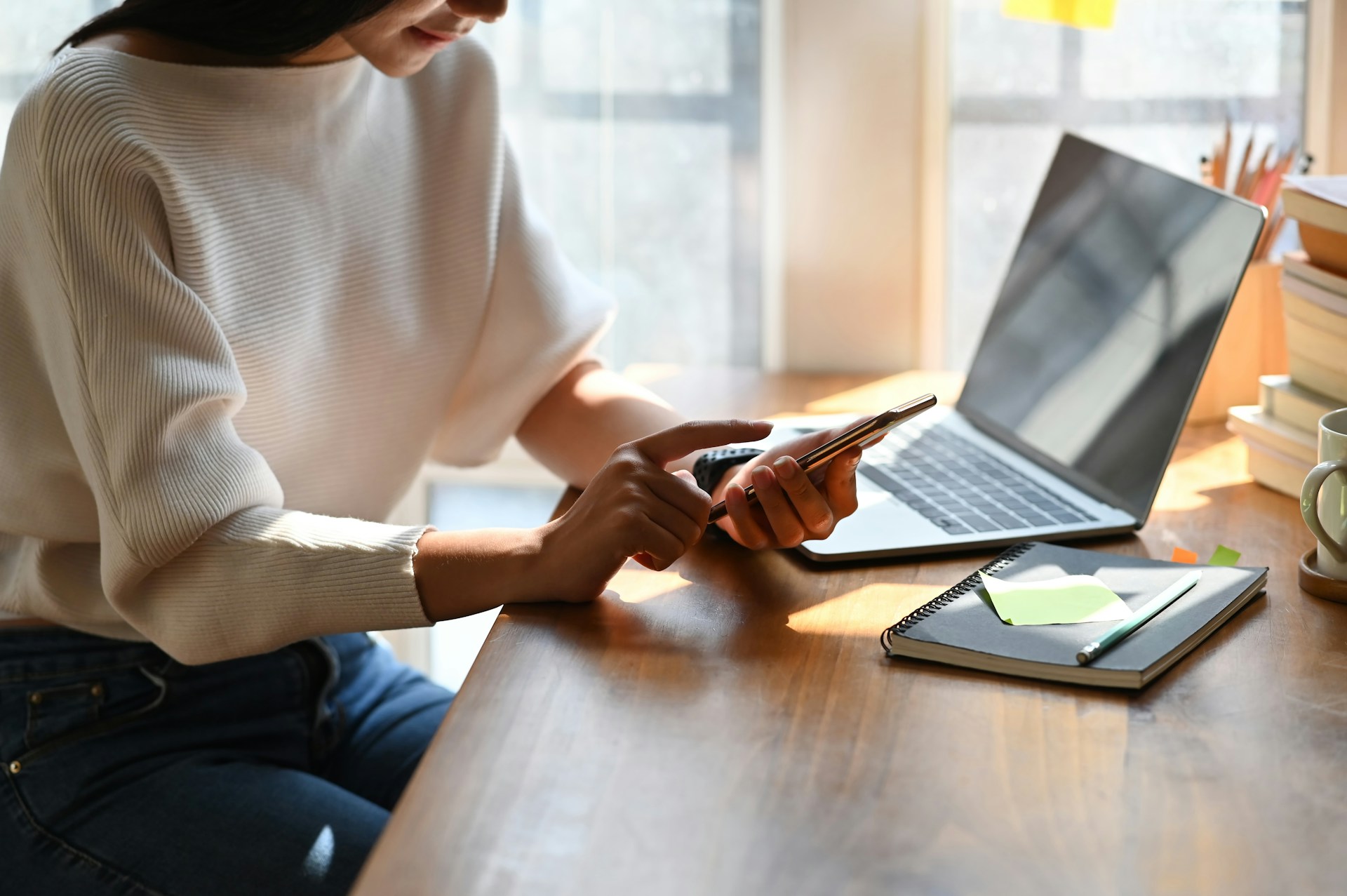 A person typing on a phone in front of a laptop