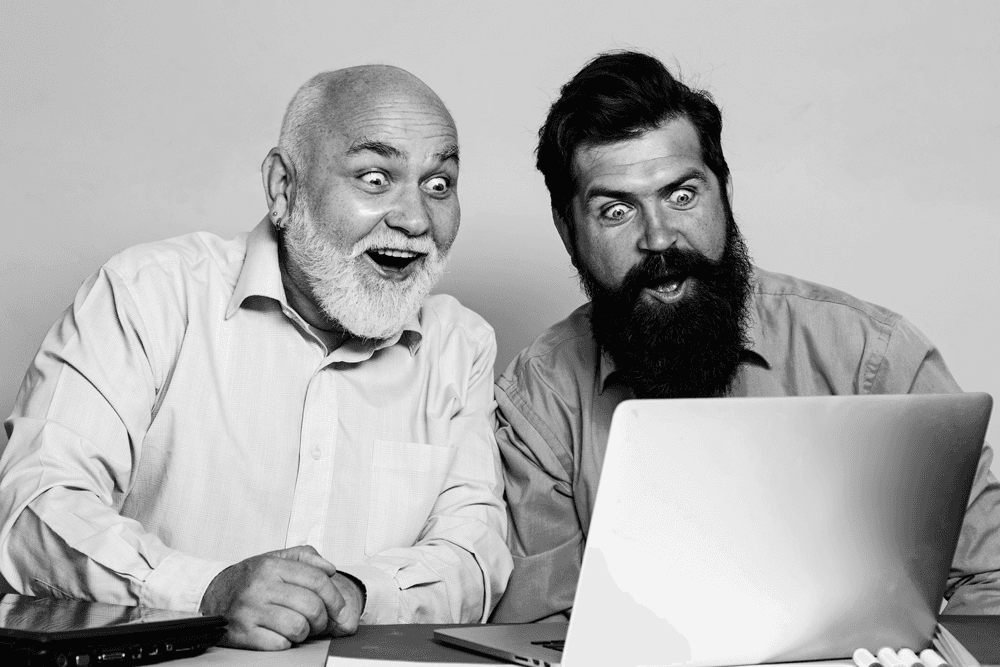 Two men discuss a project while standing at a laptop in an office.