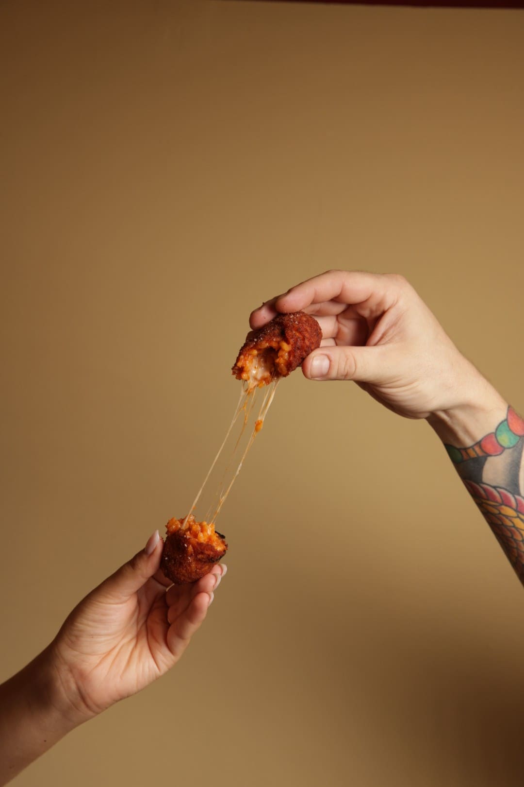 Two hands are pulling apart a piece of food, revealing a gooey, stretchy cheese texture. Background is a warm color.