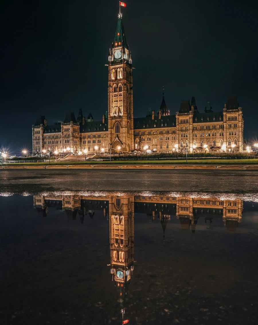 Parliament Hill at night in Ottawa, Canada, illuminated with reflections on still water.