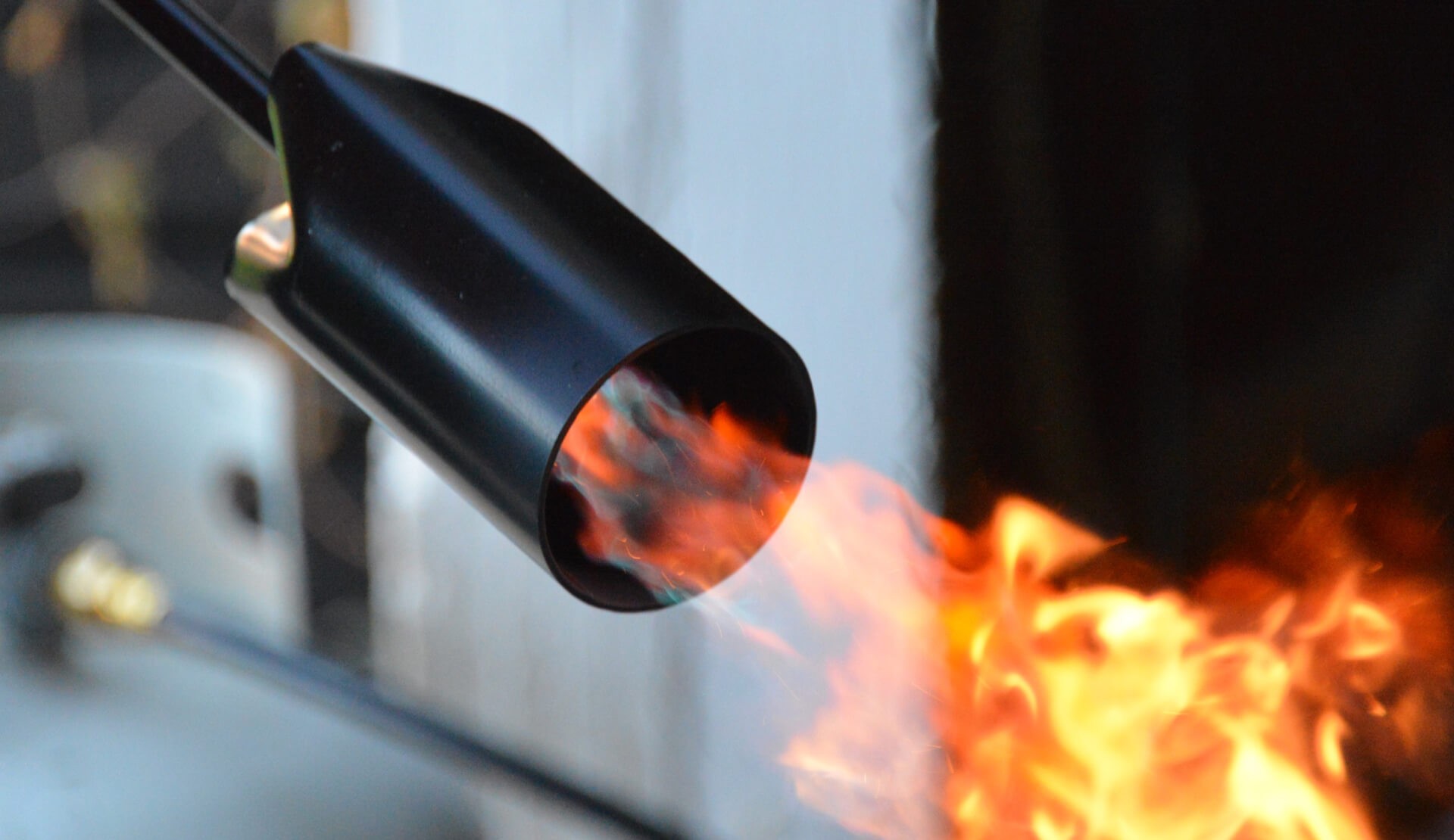 A close-up of a torch nozzle emitting flames against a background of darkened metal.