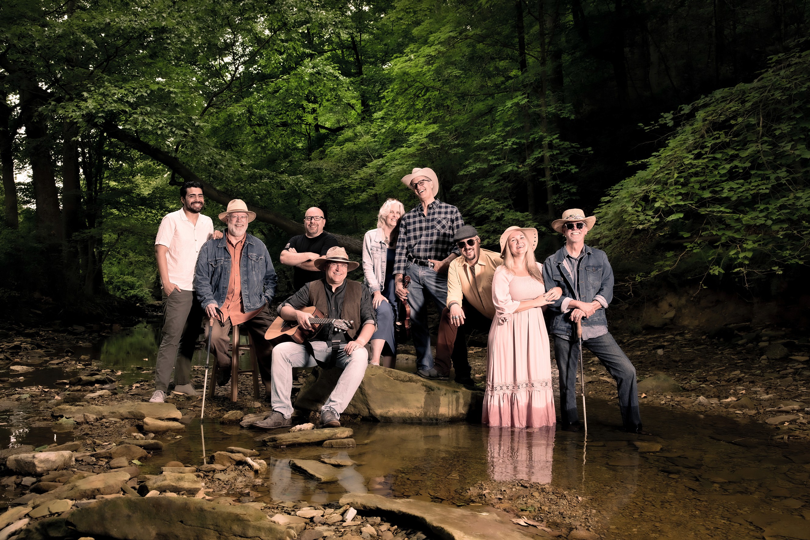 Band members posed around a large rock in the middle of a creek. They're all laughing.