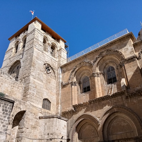 A historic stone building with arched windows and a tall bell tower, set against a clear blue sky.