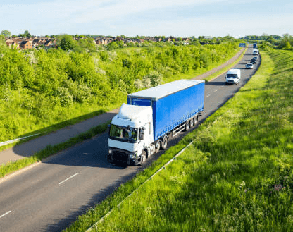 Image of a large road haulage truck driving along a road with trees and bushes either side and the trucks trailer is blue