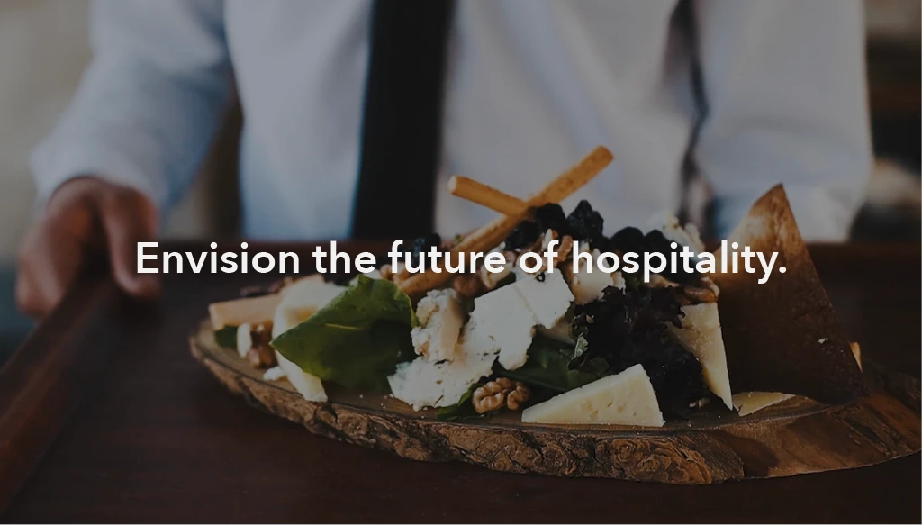An image of a waiter holding an aesthetic cheese board with the text 'envision the future of hospitality' inlayed