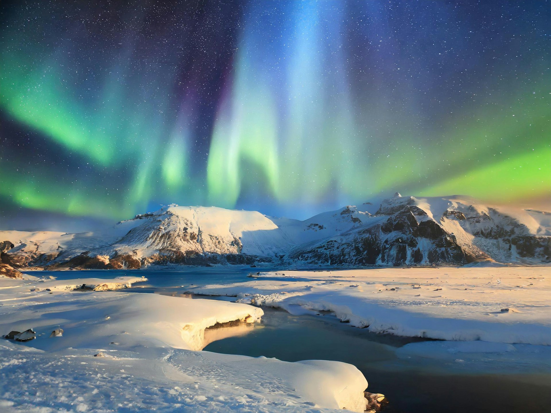 Northern lights dancing above snow-covered mountains and a frozen river in Iceland during a clear winter night.
