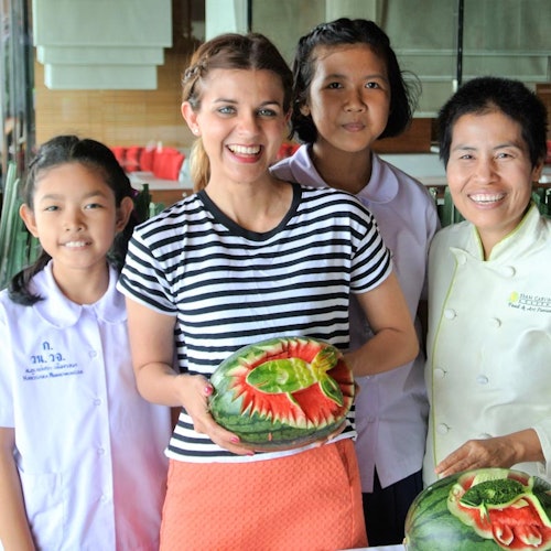 Patru persoane stau în picioare și zâmbesc, cu una dintre ele ținând un pepene verde sculptat. Mai mulți pepeni verzi sculptați sunt pe masă.