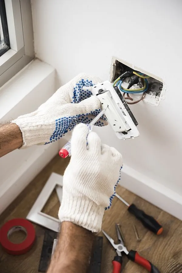 An electrician working on a wall socket with wires exposed.