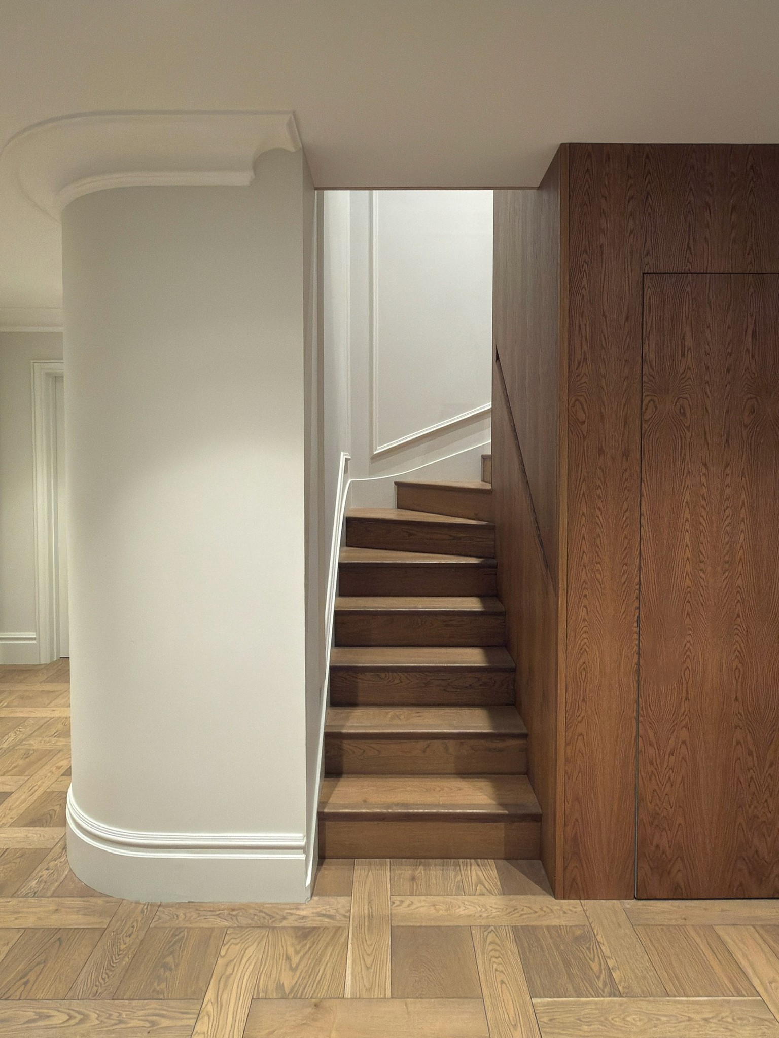 Curved white staircase hallway with oak flooring and warm timber cladding and door