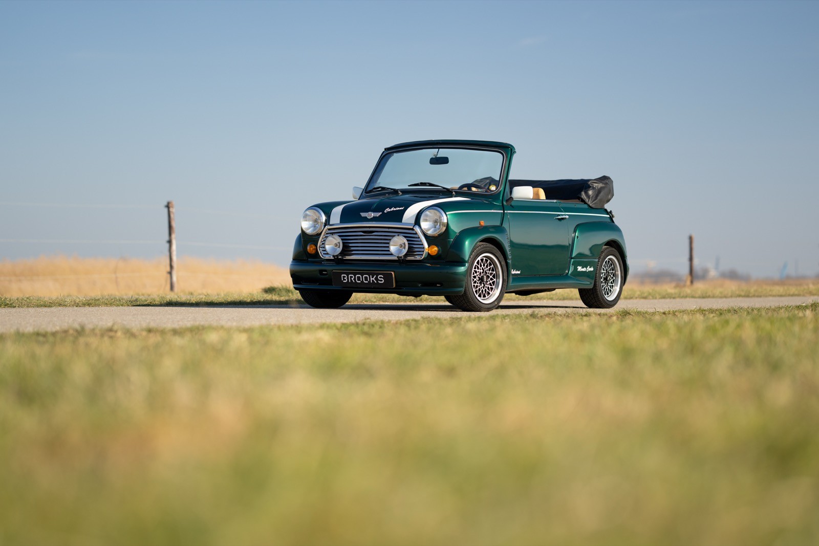 A green vintage pickup truck parked on a rural road with a clear blue sky and fields in the background.