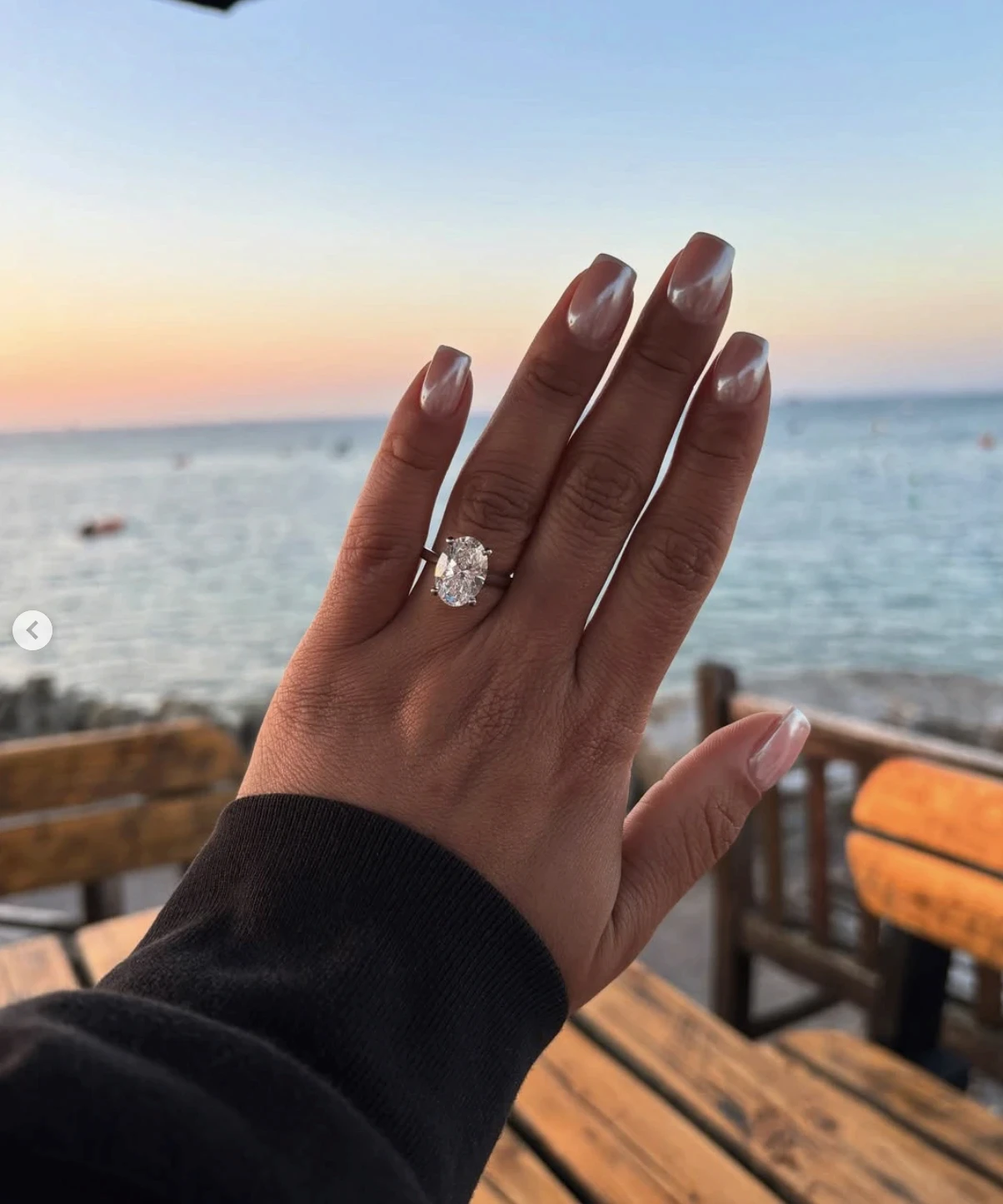 An engagement ring held up against a sunset over the sea