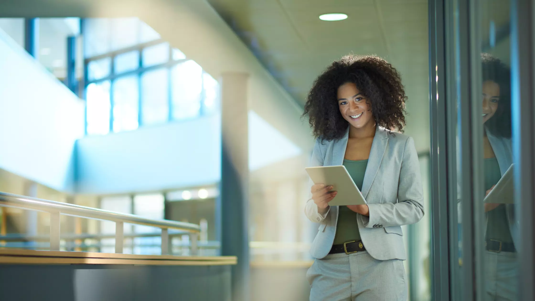 A man stands while two people sit at a table in an office setting, smiling and engaged in conversation. The mood is friendly and collaborative.