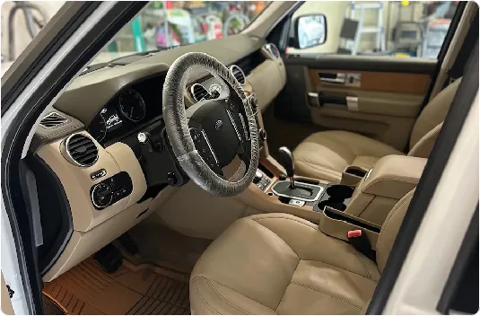 Freshly detailed front interior of an SUV showcasing perfectly clean and conditioned tan leather seats, a detailed center console, and steering wheel protection after a professional mobile car detailing service.