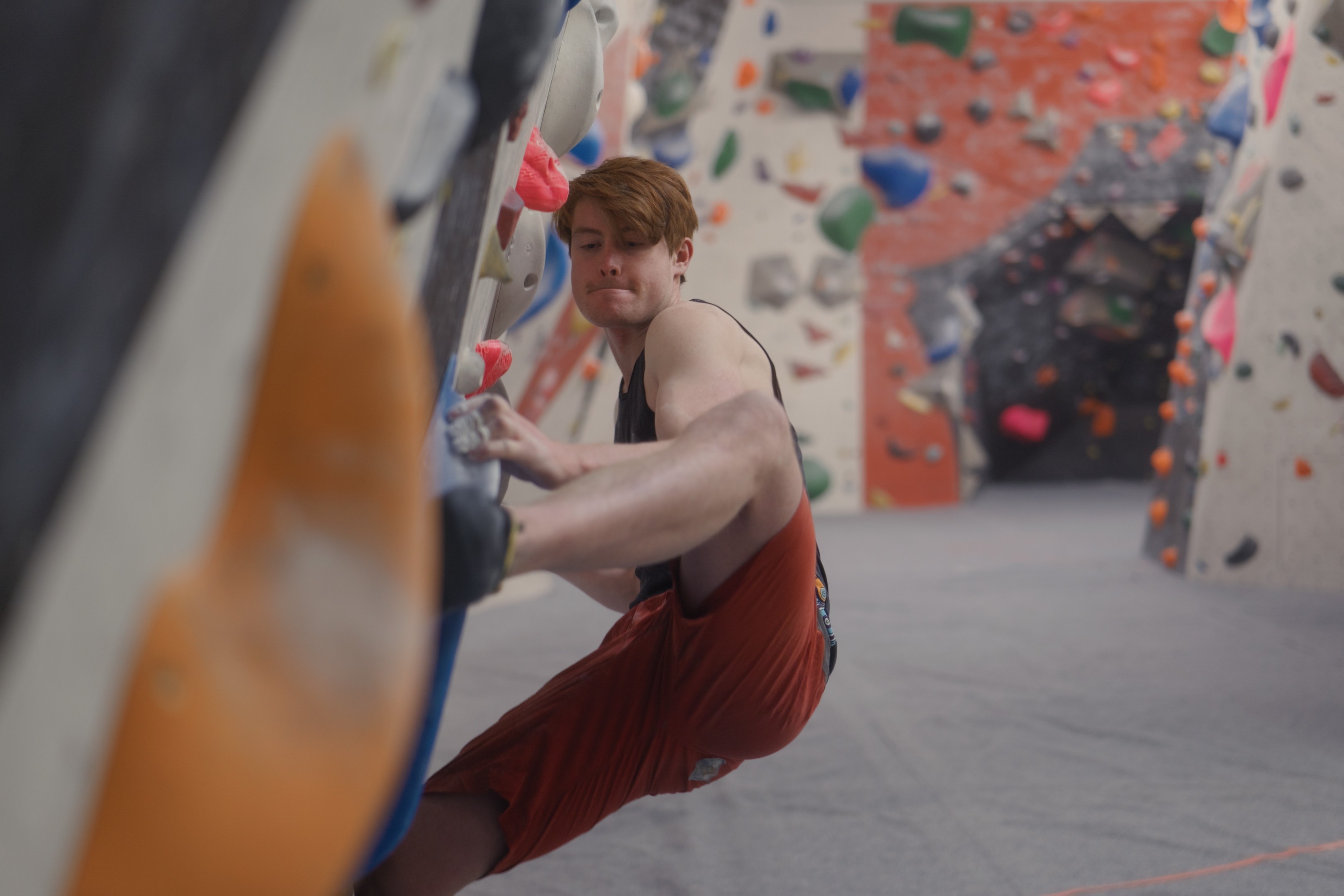 A climber focuses intently as they climb a bouldering wall, surrounded by bright, colorful holds.
