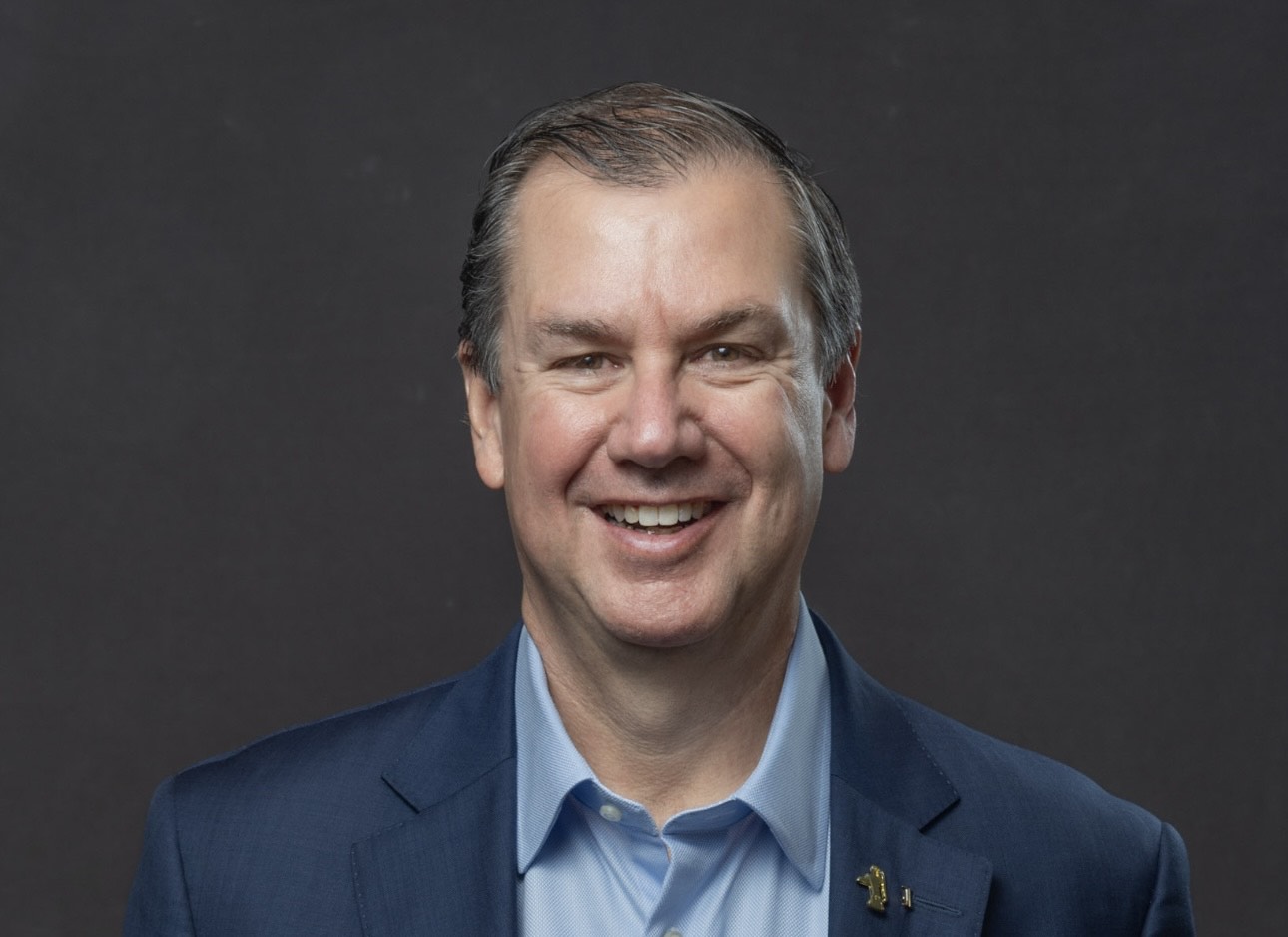 Moody portrait of a woman with straight dark hair and bangs leaning against a turquoise and pink wall, illuminated by soft natural light.